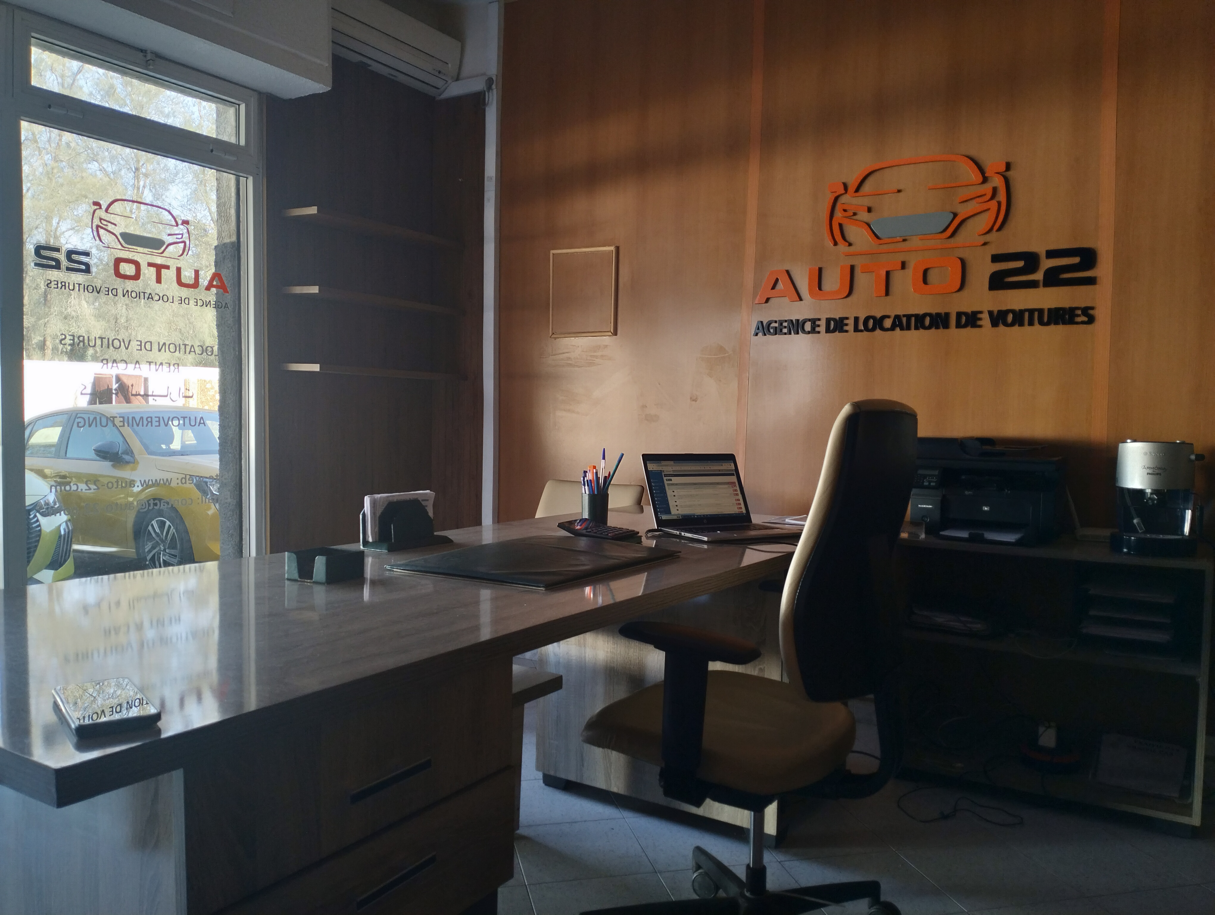 Le bureau auto 22 agadir à Agadir : plan de travail avec ordinateur portable et le logo de l'agence au mur